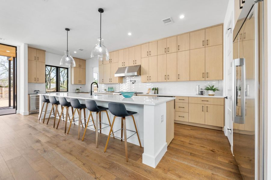 Kitchen with light brown cabinetry, visible vents, under cabinet range hood, and stainless steel built in fridge