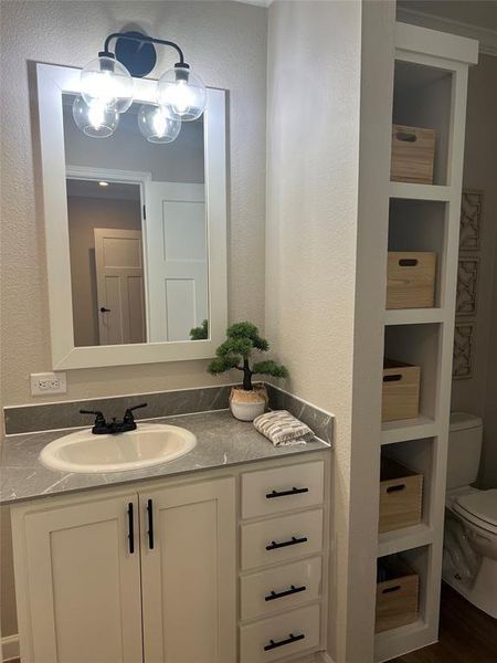 Half bathroom featuring a textured wall, vanity, and dark wood-style flooring