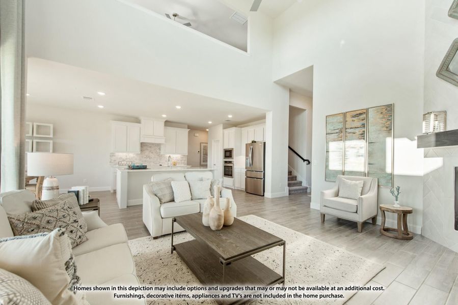 Open-concept living room with high ceilings, neutral furnishings, and white kitchen with stainless appliances in background