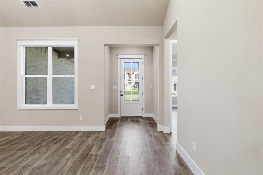 Interior entry area featuring wood-finish flooring, light neutral wall tones, white baseboards, and a white paneled door with glass inserts
