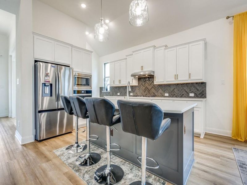Kitchen featuring an island with sink, light countertops, appliances with stainless steel finishes, white cabinets, and decorative backsplash