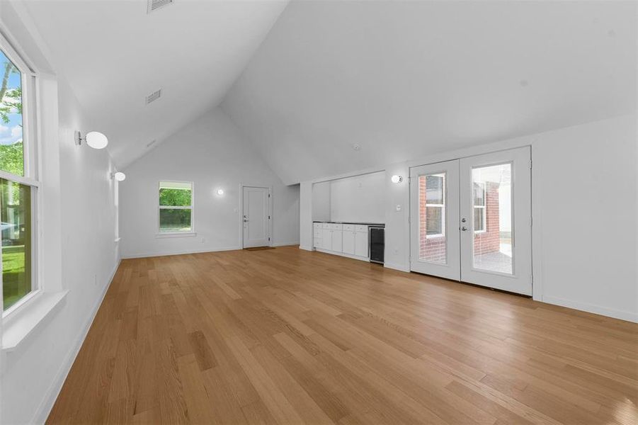 Unfurnished living room featuring french doors, lofted ceiling, and light hardwood / wood-style floors