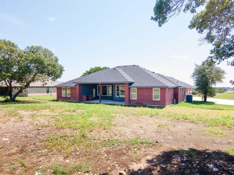 Back of property featuring a patio area, a lawn, a shingled roof, and brick siding