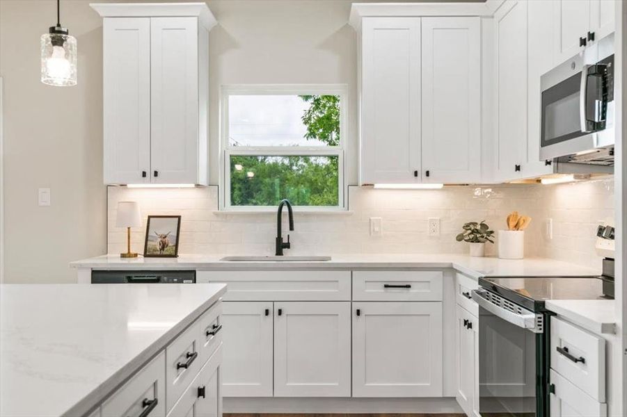 Bright kitchen featuring white shaker cabinetry with dark hardware, a single basin sink with a black gooseneck faucet, light-toned countertops, and a white subway tile backsplash with under-cabinet lighting