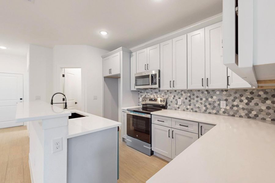 Kitchen with stainless steel appliances, decorative backsplash, a kitchen island with sink, light wood-type flooring, and recessed lighting