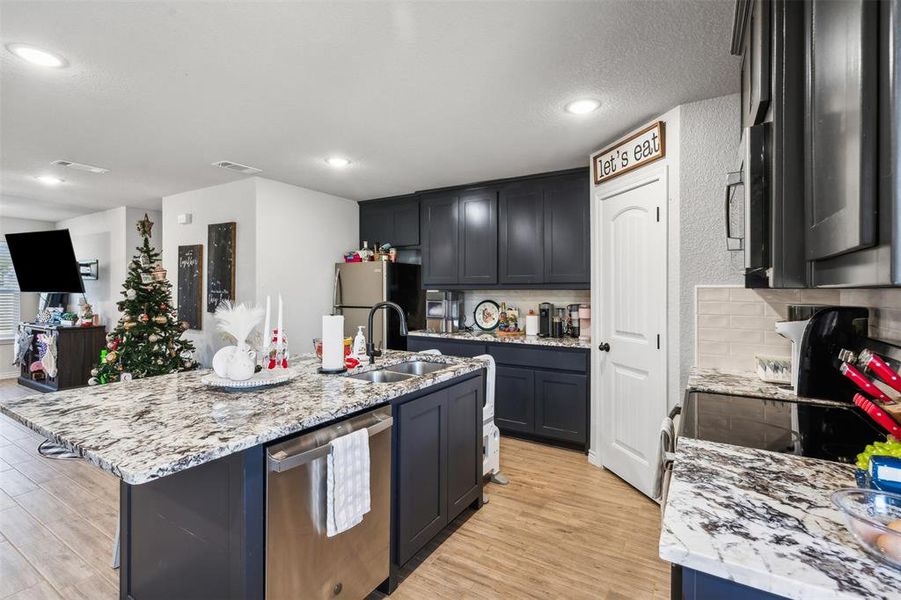 Kitchen featuring sink, stainless steel appliances, light hardwood / wood-style floors, and an island with sink