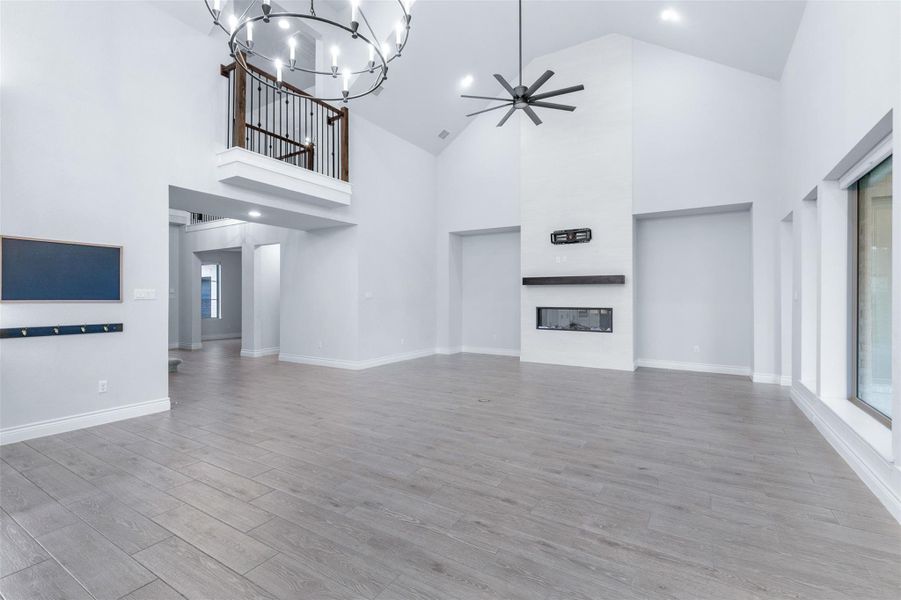 Unfurnished living room featuring a ceiling fan, light wood-style flooring, a chandelier, a glass covered fireplace, and high vaulted ceiling