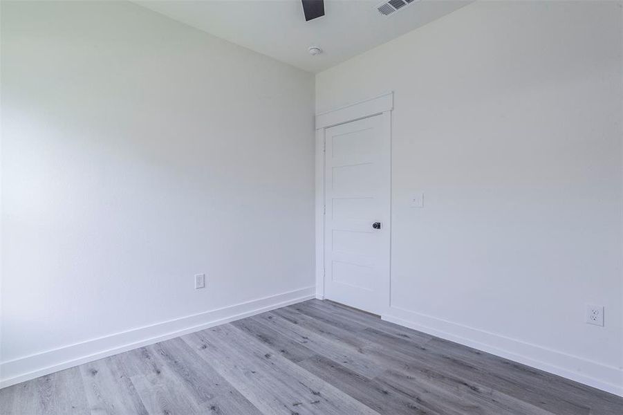 Light-filled room featuring wood-finish flooring, white baseboards, and a contemporary flat-panel door with black hardware