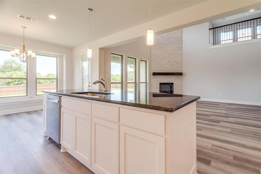 Kitchen with an island with sink, sink, a stone fireplace, and light hardwood / wood-style floors