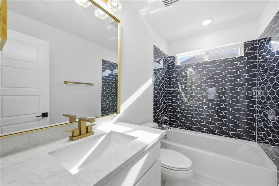Bathroom featuring a white vanity with an integrated sink, gold-tone faucet, and a large framed mirror