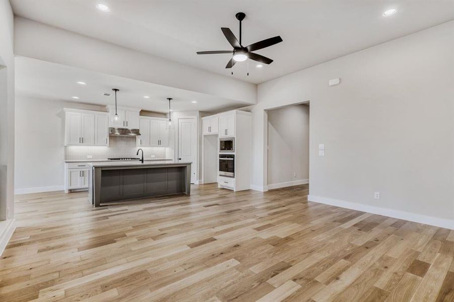 Kitchen featuring open floor plan, ceiling fan, a kitchen island with sink, light countertops, and two tone cabinetry