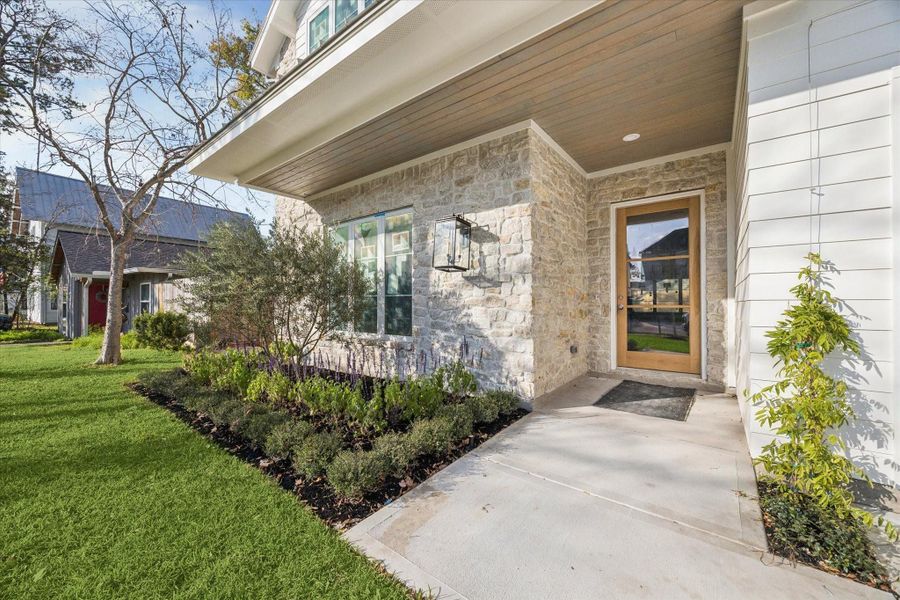 Stone wrapped entry and covered front porch create a warm, welcoming approach, highlighted by modern lantern lighting, natural textures, and thoughtful landscaping that adds privacy and curb appeal right from the sidewalk. -- Construction as of 1/5/26