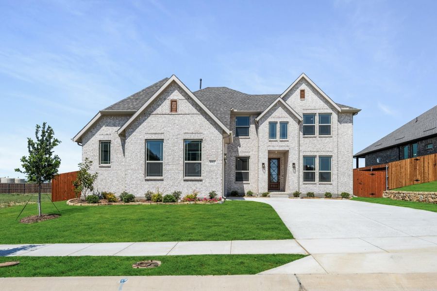 Two-story home with light brick exterior, gray roof, and concrete driveway with green lawn Two-story home with light brick exterior, gray roof, and concrete driveway with green lawn