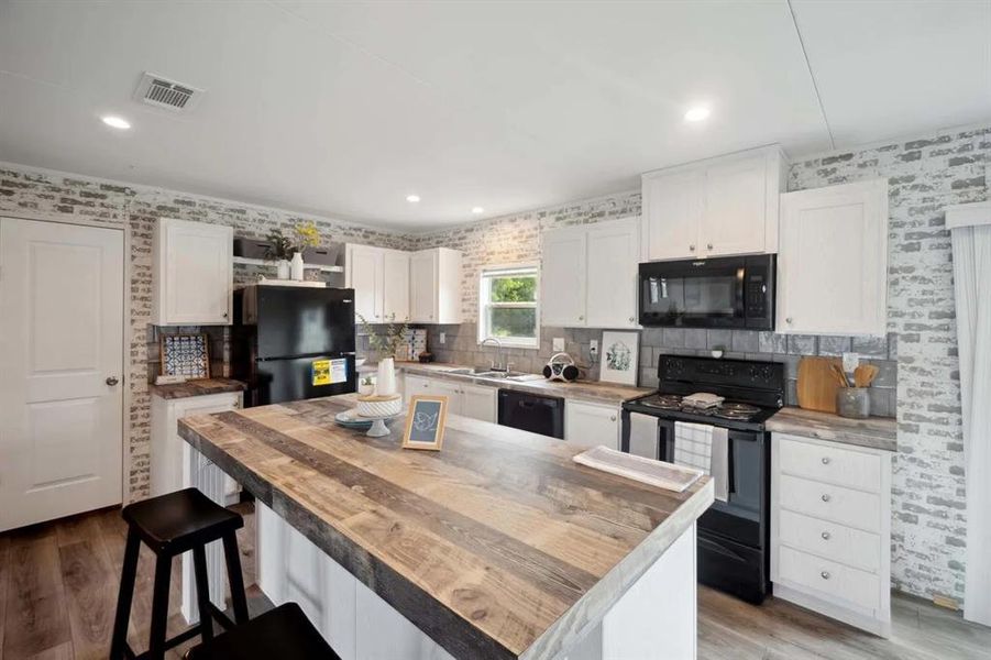 Kitchen with wooden counters, light wood-type flooring, sink, black appliances, and white cabinetry