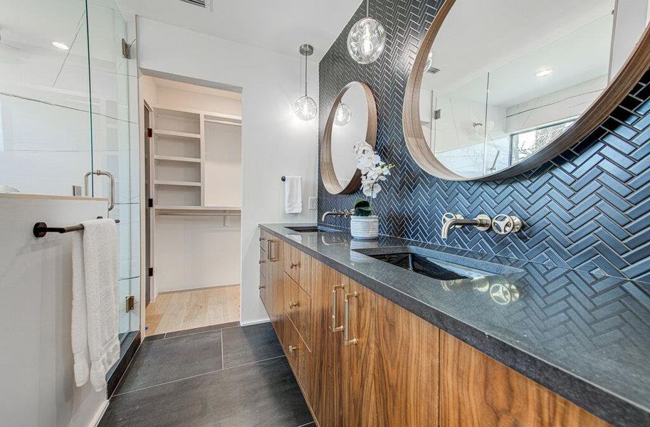 Bathroom with double vanity, a shower stall, a walk in closet, and a sink