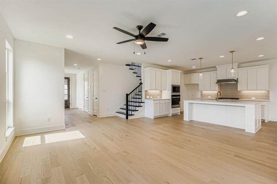 Unfurnished living room featuring light wood-style floors, stairway, ceiling fan, and recessed lighting