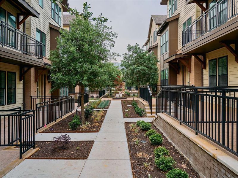 Community pathway featuring mature trees, landscaped planting beds, and brick retaining walls