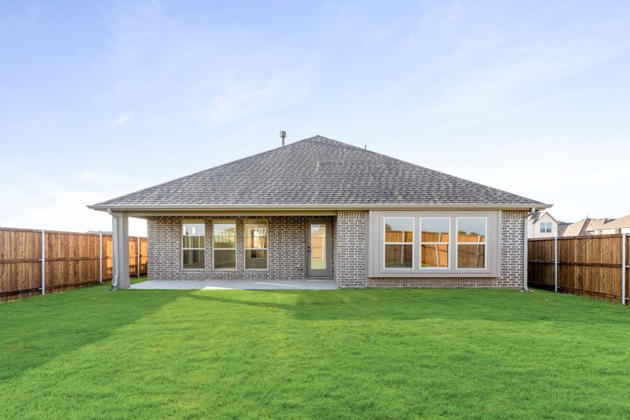 Rear exterior of single-story brick home with covered patio, large windows, and fenced backyard with green lawn Rear exterior of single-story brick home with covered patio, large windows, and fenced backyard with green lawn