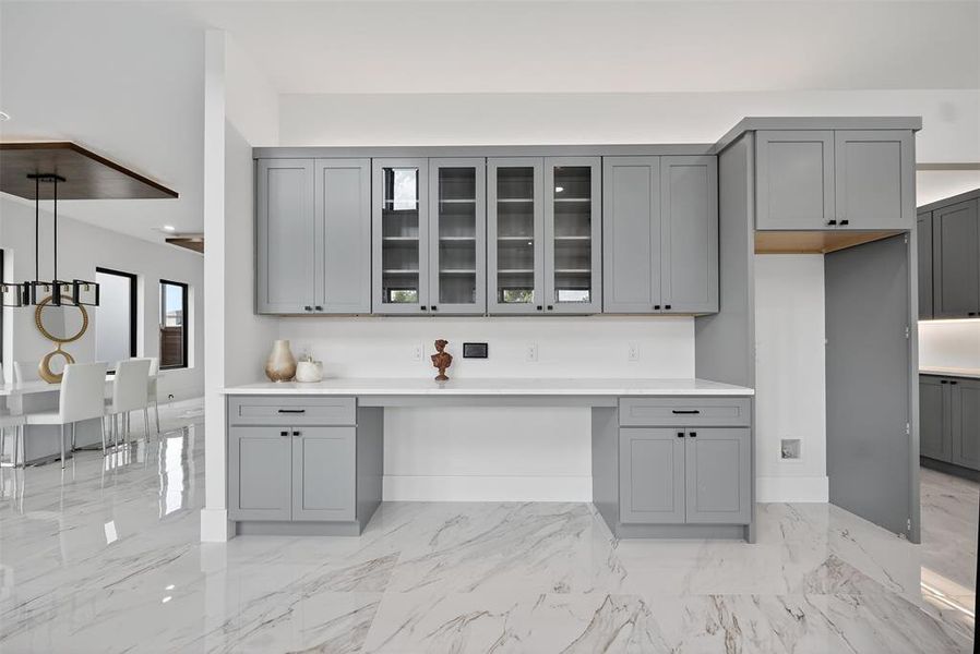 Kitchen featuring gray cabinetry, light marble finish flooring, glass insert cabinets, decorative light fixtures, and light stone counters