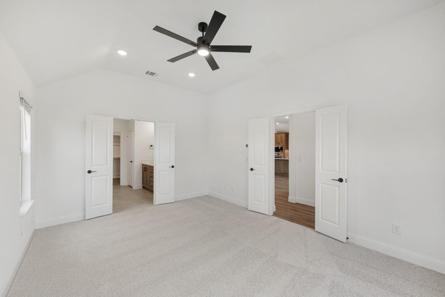 Empty bedroom with vaulted ceiling, ceiling fan, carpet floors, and doors leading to bathroom and closet Empty bedroom with vaulted ceiling, ceiling fan, carpet floors, and doors leading to bathroom and closet