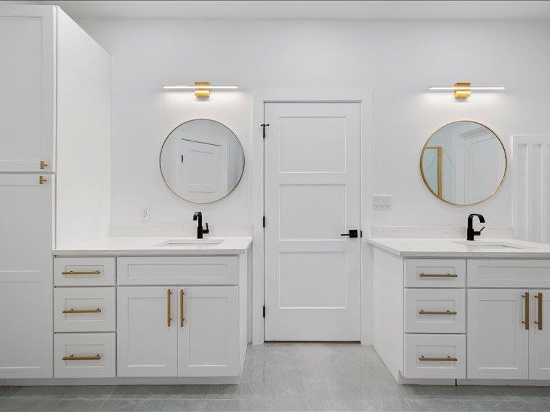 Bathroom featuring a double vanity with white cabinetry, gold hardware, and round mirrors