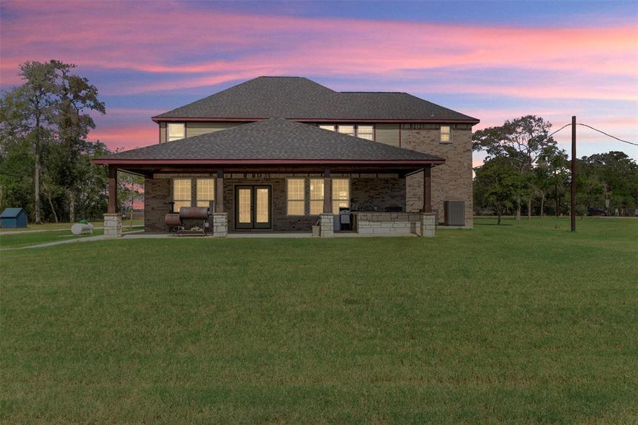 This photo showcases a two-story brick house with a spacious backyard and a covered patio, perfect for outdoor activities. It’s set against a beautiful sunset sky, offering a serene and inviting atmosphere.