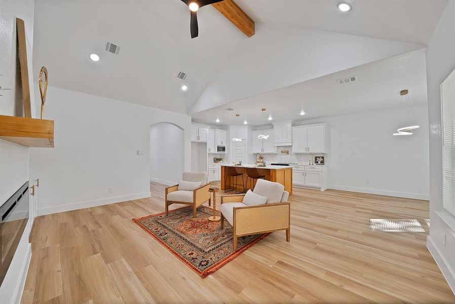 Living area with beam ceiling, arched walkways, light wood-style floors, recessed lighting, and a ceiling fan