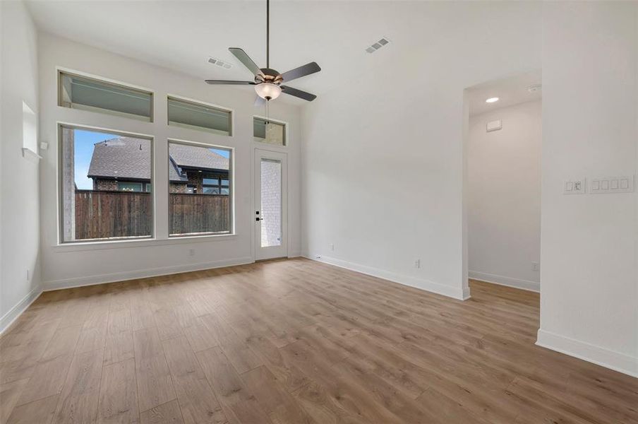 Spacious room featuring multiple windows, wood-finish flooring, a ceiling fan with integrated lighting, recessed ceiling lighting, and a white paneled door with frosted glass