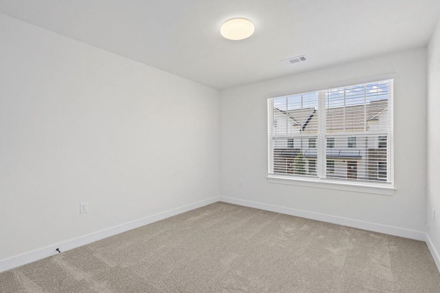 Bright room featuring a large window with blinds, light-colored carpet flooring, white walls, and a flush-mount ceiling light fixture