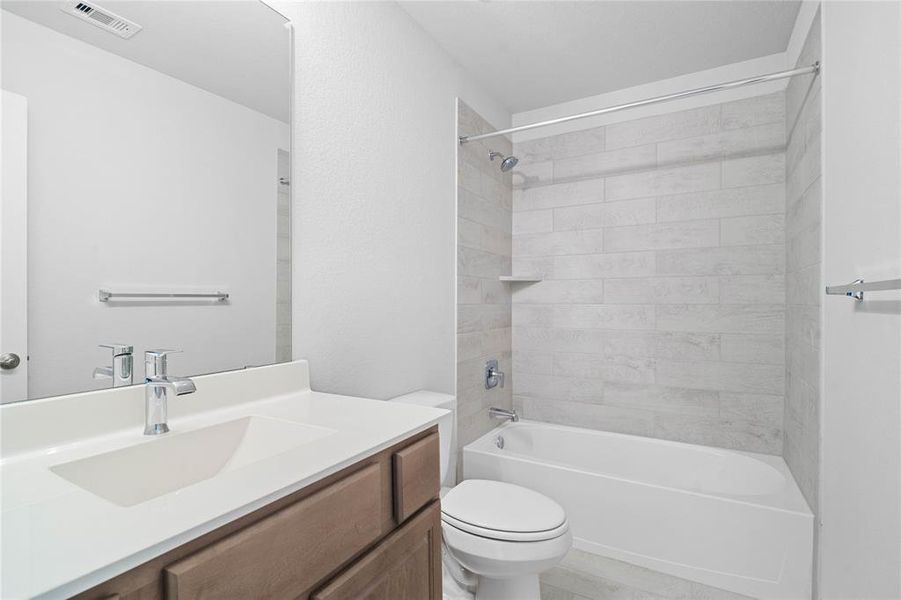 Secondary bath features tile flooring, bath/shower combo with tile surround, wood stained cabinets, beautiful light countertops, mirror, dark, sleek fixtures and modern finishes!