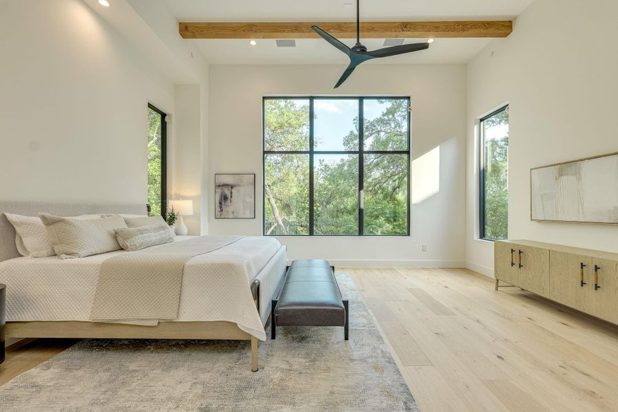 Tree-lined views fill this airy bedroom, showcasing high ceilings with an exposed beam and a modern ceiling fan. Tree-lined views fill this airy bedroom, showcasing high ceilings with an exposed beam and a modern ceiling fan.