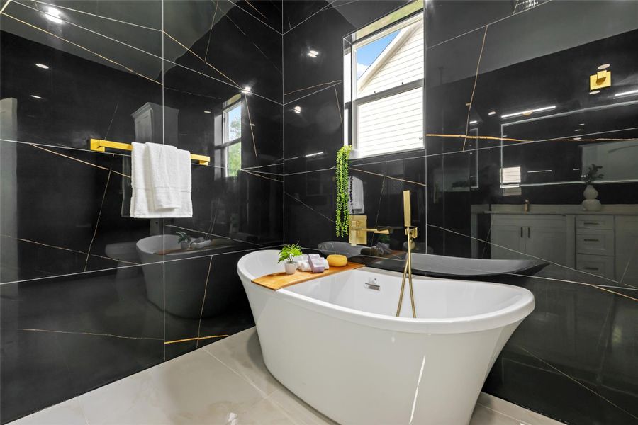 Freestanding soaking tub set against black marble-look wall tiles with gold veining