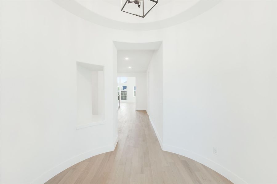 Curved entryway with round tray ceiling, pendant light, hardwood floors, and built-in wall niche leading to hallway