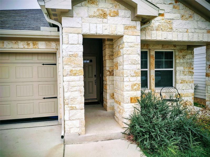Property entrance with stone siding, an attached garage, and roof with shingles