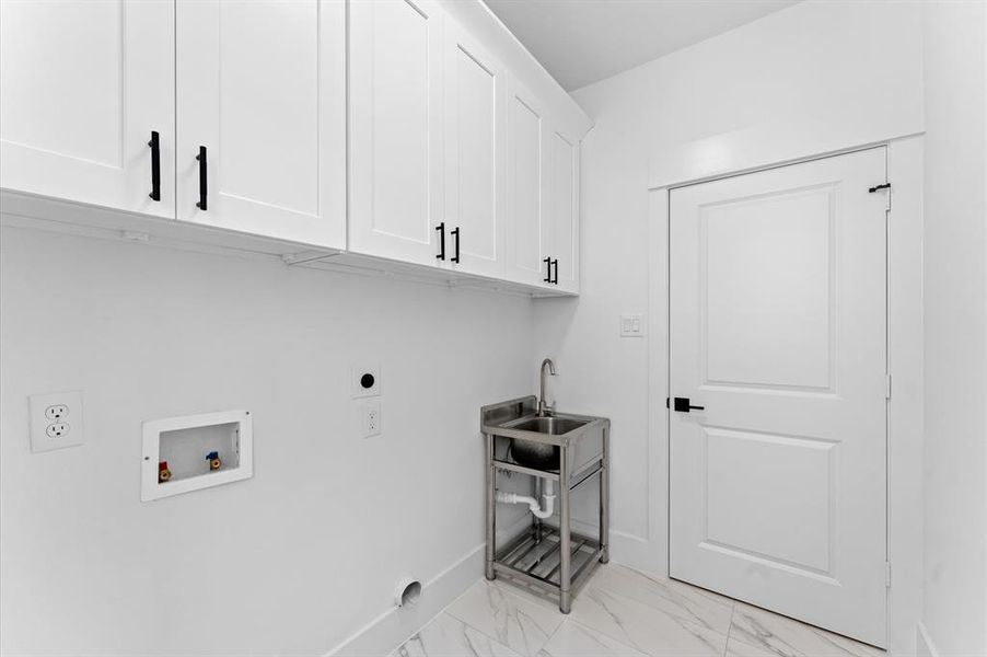 This photo shows a bright laundry room with white cabinetry, a utility sink, and hookups for a washer and dryer. The space has modern finishes and tiled flooring, creating a clean and functional area.