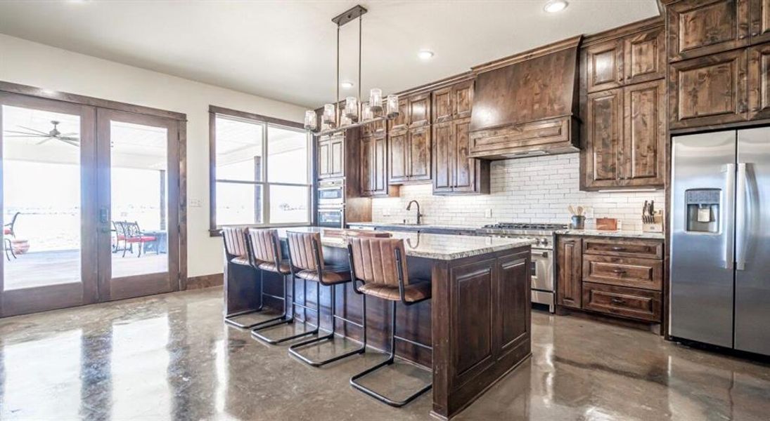 Kitchen with decorative backsplash, dark brown cabinets, stainless steel appliances, a breakfast bar area, and concrete floors Kitchen with decorative backsplash, dark brown cabinets, stainless steel appliances, a breakfast bar area, and concrete floors