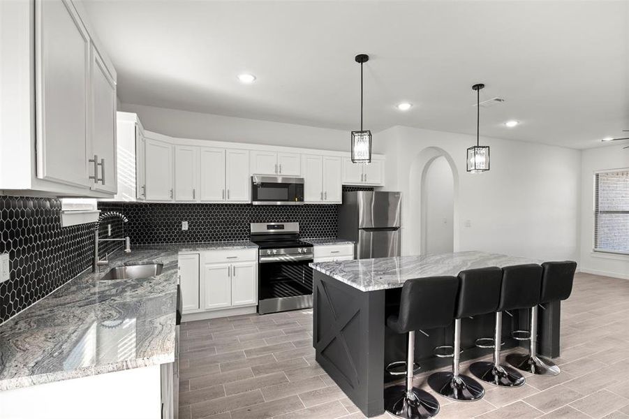 Kitchen with white cabinetry, stainless steel appliances, light stone countertops, backsplash, and decorative light fixtures