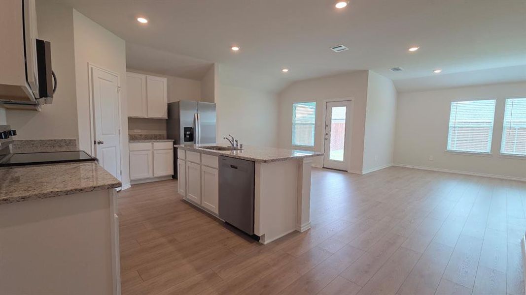 Open-concept kitchen and living area featuring wood-finish flooring, recessed lighting, and white cabinetry