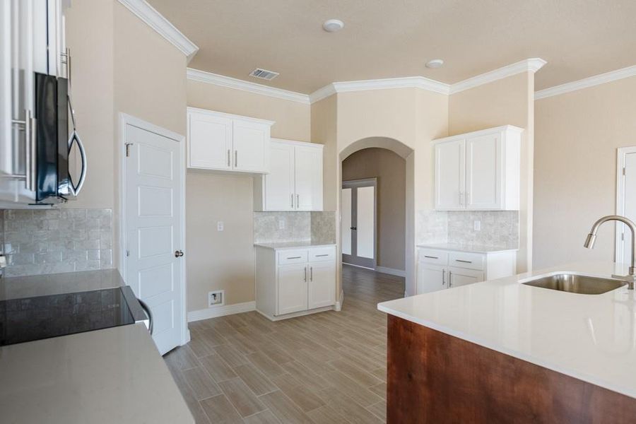 Kitchen featuring white cabinets, arched walkways, tasteful backsplash, light stone countertops, and ornamental molding Kitchen featuring white cabinets, arched walkways, tasteful backsplash, light stone countertops, and ornamental molding
