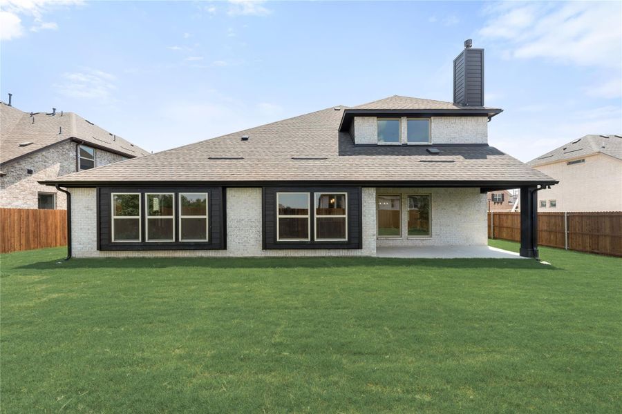 Rear exterior of brick home with covered patio, large windows, and fenced backyard with green lawn Rear exterior of brick home with covered patio, large windows, and fenced backyard with green lawn
