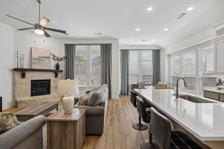 Open-concept living space featuring wood-finish flooring, a stone-surround fireplace with a dark wood mantel, and large windows with blinds
