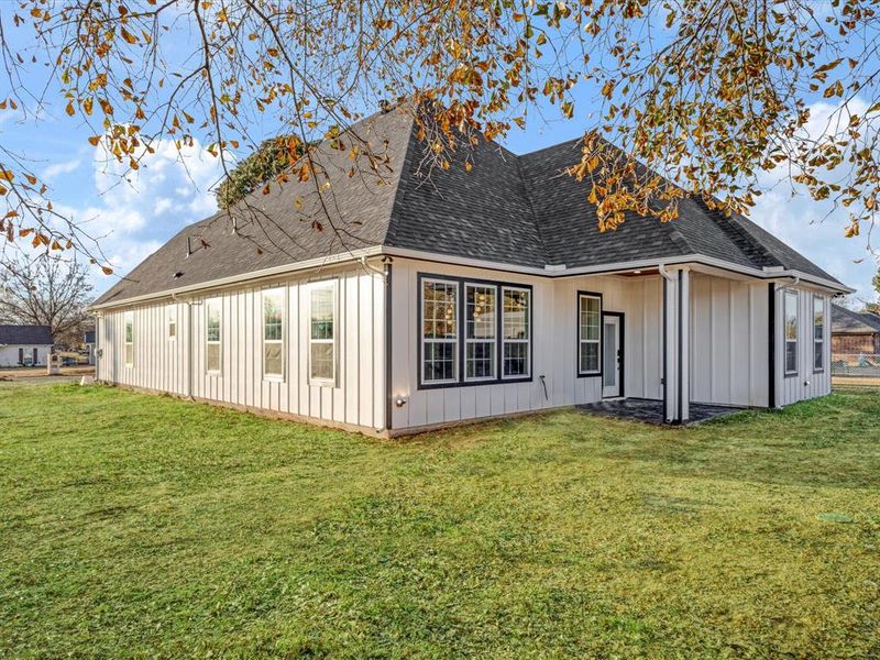 Back of house featuring a patio, a lawn, roof with shingles, and board and batten siding Back of house featuring a patio, a lawn, roof with shingles, and board and batten siding