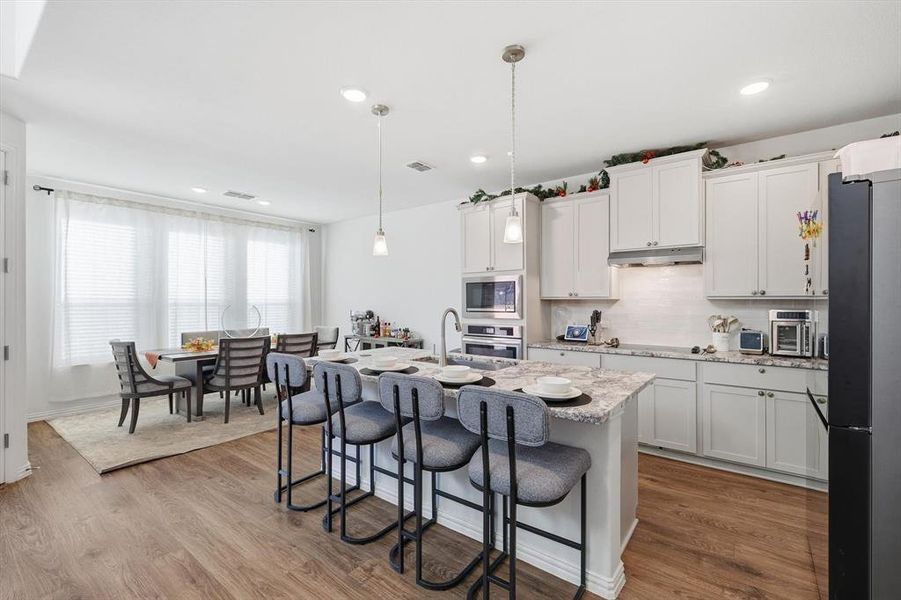 Kitchen featuring a kitchen bar, hanging light fixtures, white cabinetry, stainless steel appliances, and recessed lighting
