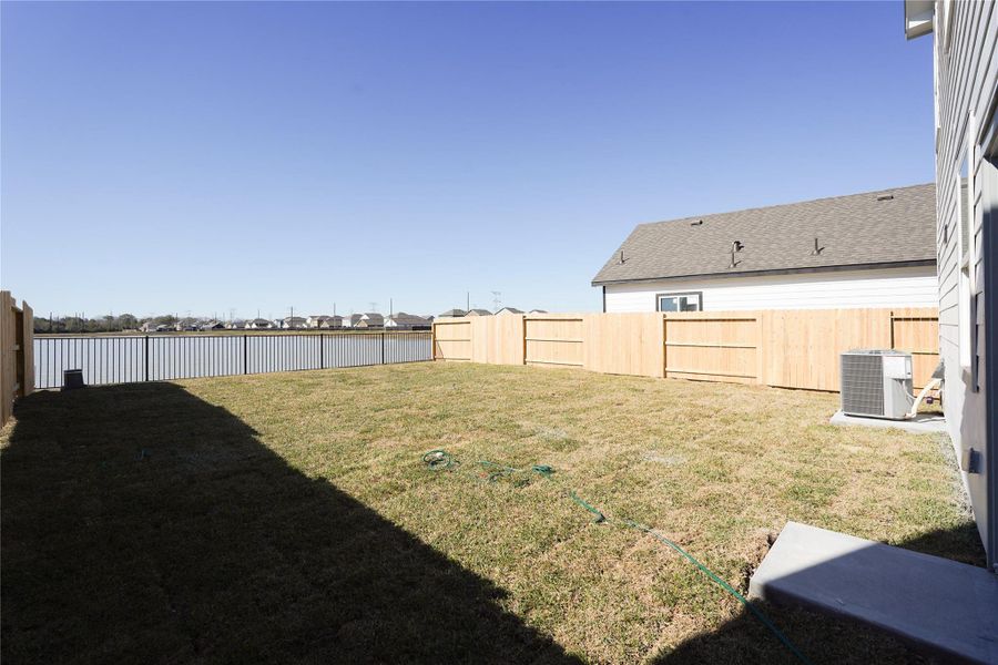 Spacious backyard with a well-maintained lawn, wooden fencing for privacy, and a view of a nearby lake, perfect for outdoor activities and relaxation.