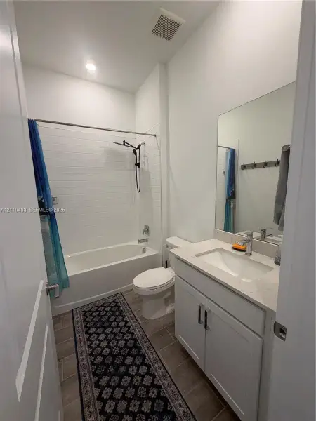 Bathroom featuring a vanity with a stone-finish countertop, undermount sink, and shiplap-style tile shower surround with a matte black rainfall showerhead