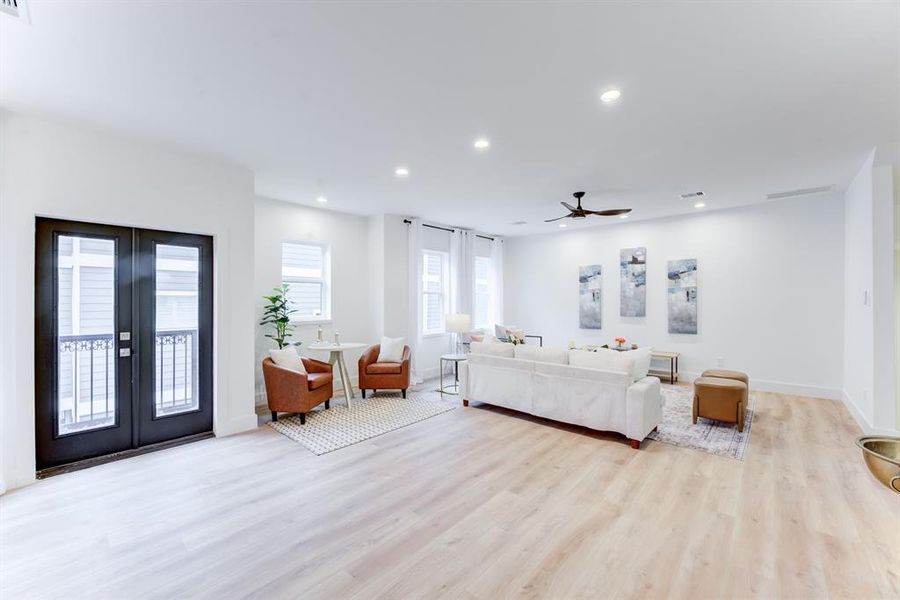 This spacious living room features an open layout with light wood flooring, modern decor, and ample natural light from large windows and double door balcony.