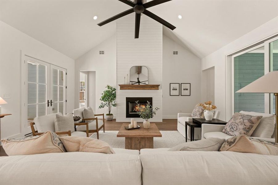 Living room with wood finished floors, a large fireplace, french doors, high vaulted ceiling, and recessed lighting Living room with wood finished floors, a large fireplace, french doors, high vaulted ceiling, and recessed lighting