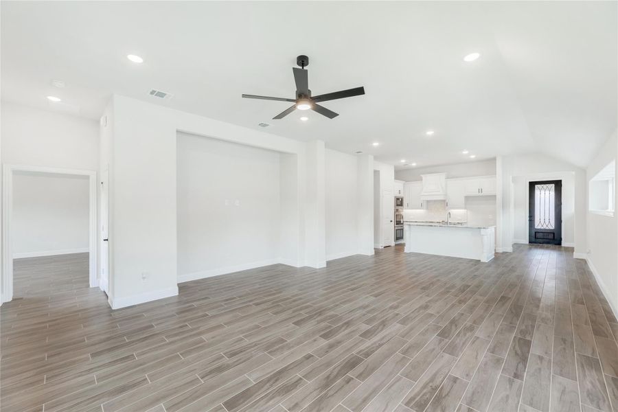 Open living area with wood-look tile floors, ceiling fan, and open kitchen with white cabinets in background Open living area with wood-look tile floors, ceiling fan, and open kitchen with white cabinets in background