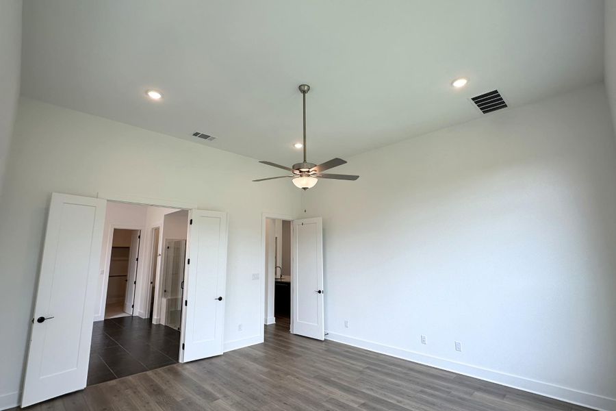 A spacious primary bedroom featuring high ceilings, recessed lighting, and elegant wood flooring, with access to an en-suite and walk-in closet.