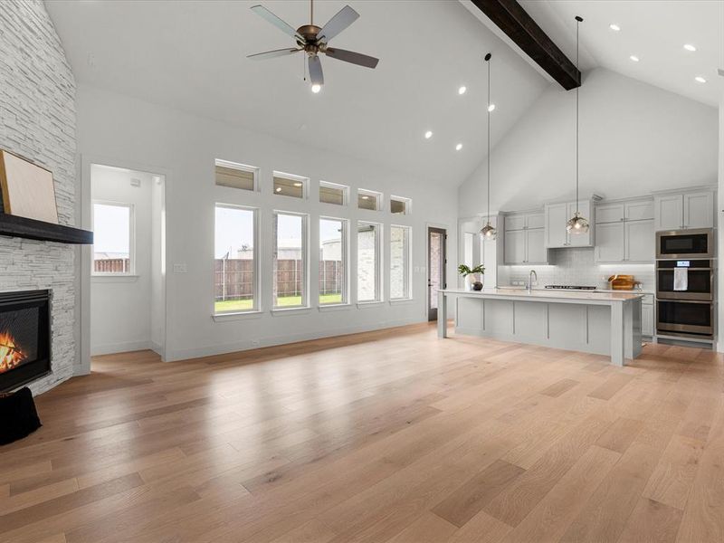 Unfurnished living room featuring high vaulted ceiling, light wood-style flooring, beam ceiling, a stone fireplace, and a ceiling fan Unfurnished living room featuring high vaulted ceiling, light wood-style flooring, beam ceiling, a stone fireplace, and a ceiling fan